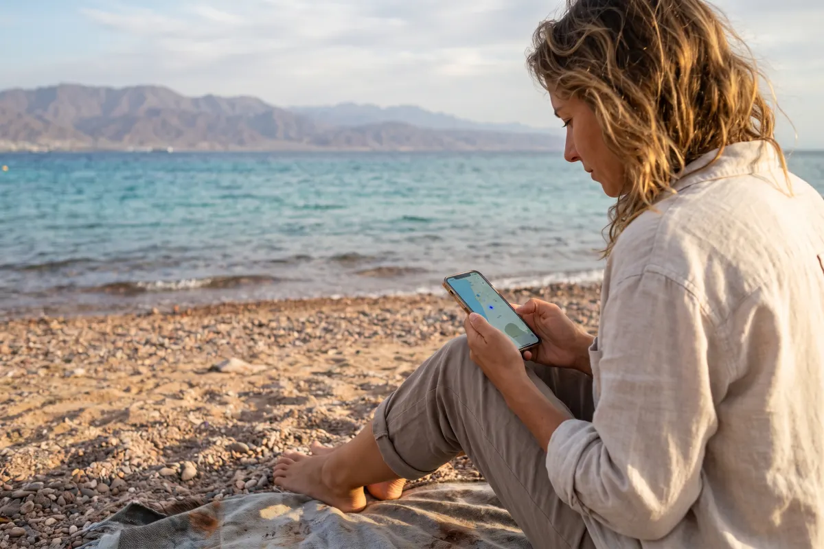 Woman checking a map on her smartphone on Eilat beach in winter sunshine