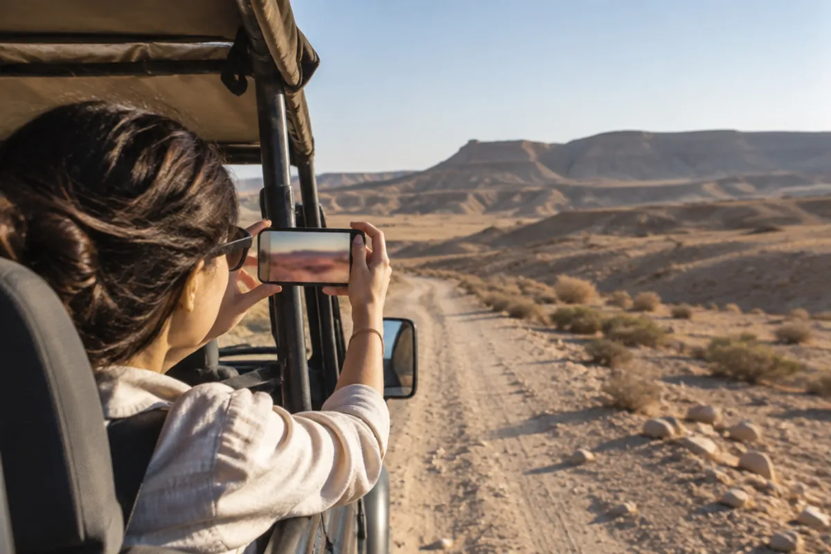A 4x4 jeep tour on a dusty track in the Negev desert, a passenger filming the landscape with a smartphone